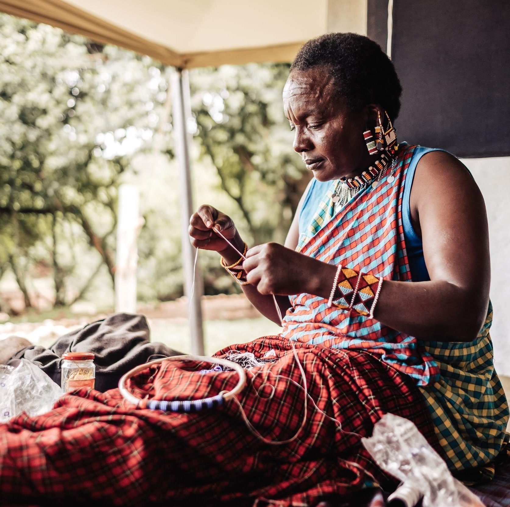 A Masai craftsperson threading a needle and beads for a necklace.