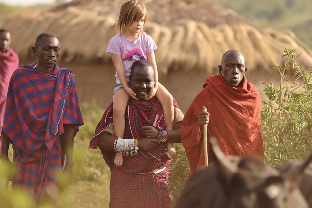 A young girl riding the shoulders of a Masaai villager during a visit