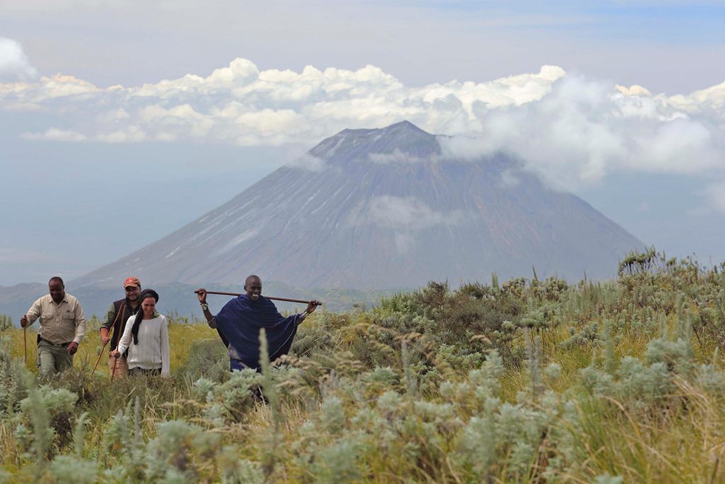 A group of visitors led by a Massai villager walking towards a mountain