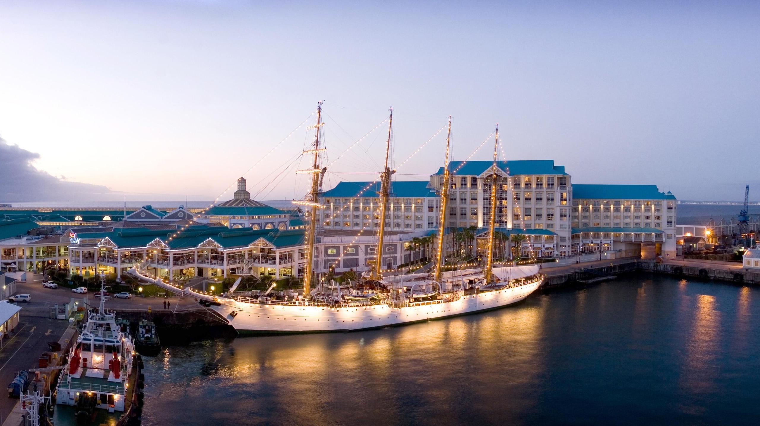 A classical sailing ship lit up by lights illuminating part of the V&A waterfront