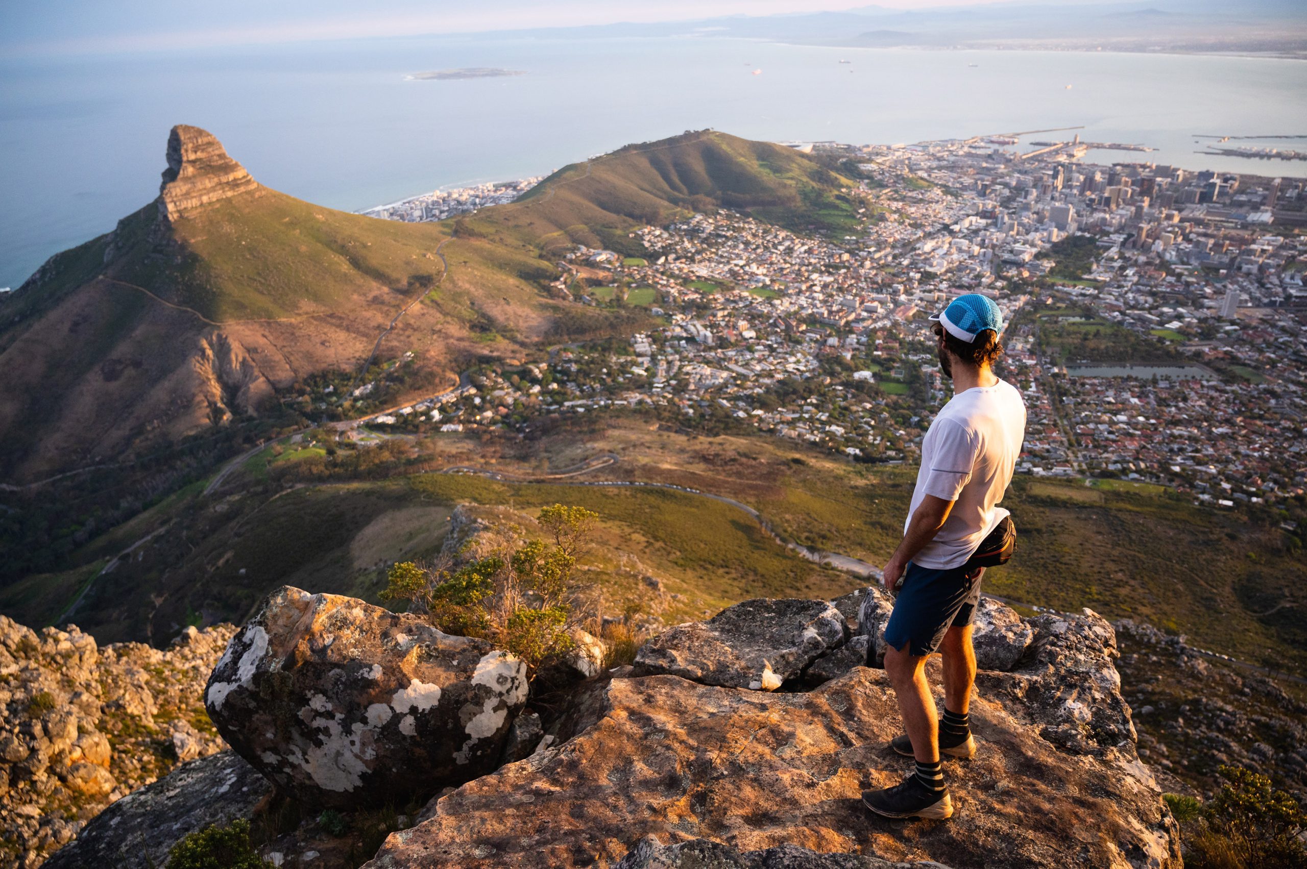 A hiker standing on a boulder looking back down across Cape Town from Table Mountain